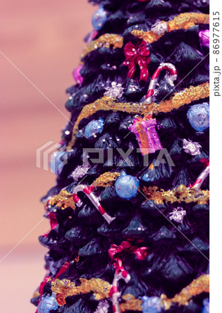 A beautifully decorated stylish ceramic Christmas tree decorated with different toys, garlands, lollipops, bows close-up at New Year's Eve 2022. Vertical photo. Trendy colors pink yellow violet toning 86977615