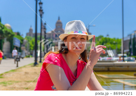 Young woman traveler with red dress and hat is sitting near fountain in Barcelona in sunny summer day 86994221