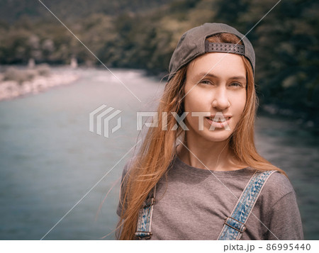 Smiling fair-haired woman squinting her eyes while standing on the background of the river valley. Close-up photo. 86995440