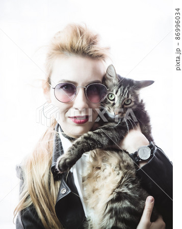 Beautiful blonde in sunglasses holds a large striped cat on a bright white background. High key 86996034