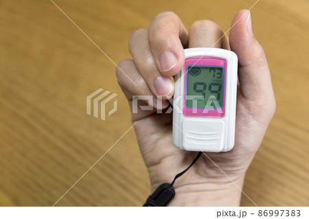 パルスオキシメーターで血中酸素飽和濃度を測定する女性手元 86997383