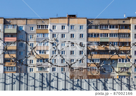 residential multi-storey building behind a fence with barbed wire at daylight, the concept of imprisonment, restriction of freedom, quarantine 87002166