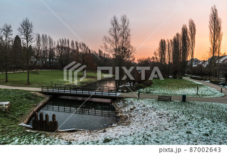 Idyllic view over a pond, bare trees and meadows covered with a thin snowlayer in the Baudouin park during sunrise, Jette Belgium 87002643