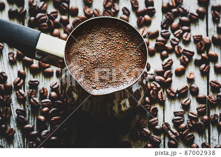 Turkish coffee in coffee pot, coffee beans scattered on wooden table, high angle view 87002938