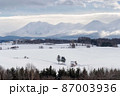 北海道・美瑛町 冬の十勝岳連峰と赤い屋根の家のある丘の風景 87003936