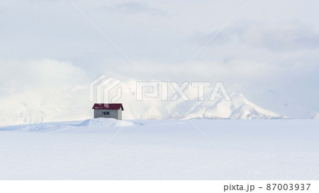 北海道・美瑛町 冬の丘に佇む小屋と背後に聳える十勝岳の風景 87003937