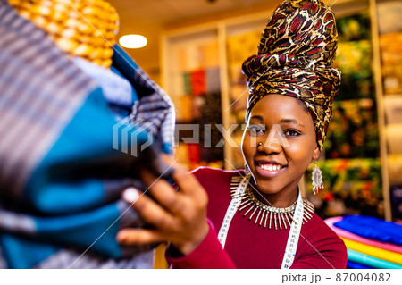 tanzanian woman with snake print turban over hear working in fabrics shop 87004082