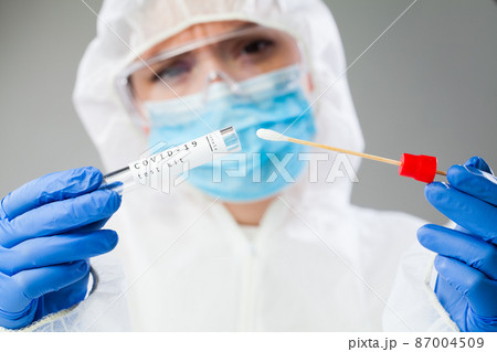 Female doctor in coveralls holding COVID-19 PCR nasal swabbing kit 87004509