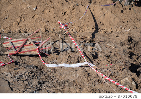 Fallen wooden fence and barrier tape. Fence with prohibition and warning signs lies on the ground. Buried ditch. Daytime. Fallen wooden fence and barrier tape. Fence with prohibition and warning signs lies on the ground. Buried ditch. Daytime. 87010079