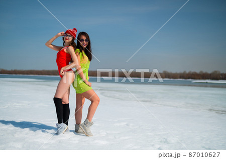 Two girlfriends in swimsuits walk along the shore of the frozen sea.  87010627