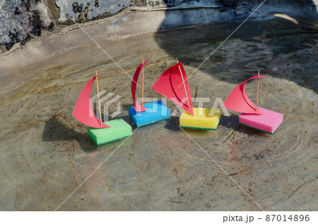 Four children's colorful ships are floating in a shallow pond. The toy sailboats are made from kitchen sponges. Summer, daytime. Selective focus. No people. 87014896