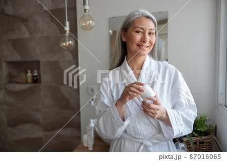 Pretty Asian woman holding cosmetic jar in the bathroom Pretty Asian woman holding cosmetic jar in the bathroom 87016065