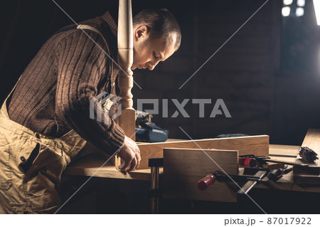 A man makes wood products with the help of special tools. Portrait of a young carpenter at work. Employment in the woodworking industry 87017922