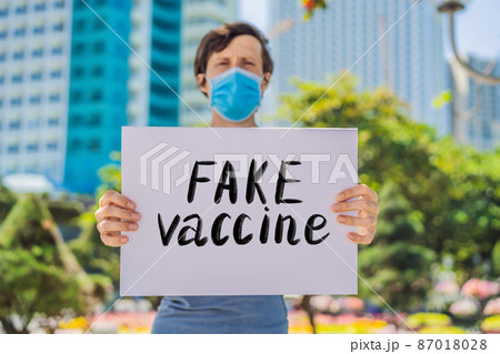 Man in medical mask prevents coronavirus disease holds a poster Fake vaccine Hand written text - lettering isolated on white. Coronovirus COVID 19 concept 87018028