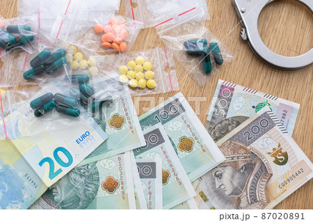 On the table lies currency in banknotes of different countries and drugs in pills and handcuffs. On the table lies currency in banknotes of different countries and drugs in pills and handcuffs. 87020891