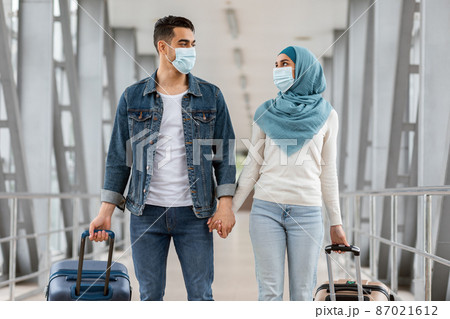 Happy Muslim Couple Wearing Protective Medical Masks Walking With Luggage At Airport Happy Muslim Couple Wearing Protective Medical Masks Walking With Luggage At Airport 87021612
