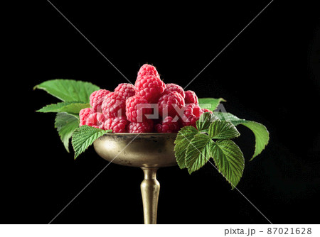 Fresh raspberries with leaves in an old brass dish. 87021628