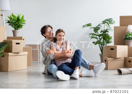 Glad millennial caucasian male in glasses and female in casual hugs, sits on floor among cardboard boxes Glad millennial caucasian male in glasses and female in casual hugs, sits on floor among cardboard boxes 87022101