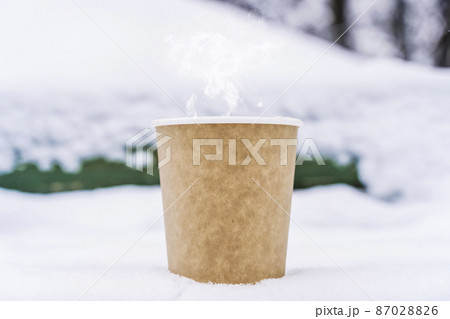 Coffee in a paper cup on a snowy winter background. Hot drink in cold weather. 87028826