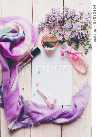 Flat lay, top view spring table desk frame. Feminine desk workspace with cosmetics, lipstick and lilac flowers on wooden background. Flat lay, top view spring table desk frame. Feminine desk workspace with cosmetics, lipstick and lilac flowers on wooden background. 87030164