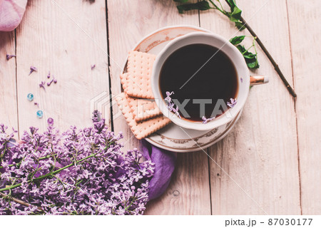Morning cup of tee, cookies, and lilac flower on wooden table from above. Beautiful breakfast. Flat lay style with copy space Morning cup of tee, cookies, and lilac flower on wooden table from above. Beautiful breakfast. Flat lay style with copy space 87030177