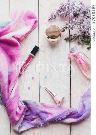 Flat lay, top view spring table desk frame. Feminine desk workspace with cosmetics, lipstick and lilac flowers on wooden background. 87030297