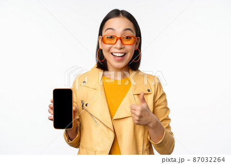 Beautiful korean girl, asian woman in sunglasses, showing smartphone app interface, thumbs up, recommending mobile phone application, white background Beautiful korean girl, asian woman in sunglasses, showing smartphone app interface, thumbs up, recommending mobile phone application, white background 87032264