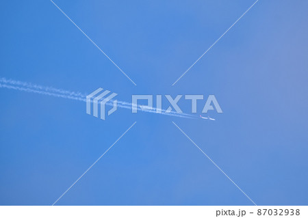 Distant passenger jet plane flying on high altitude on clear blue sky leaving white smoke trace of contrail behind. Air transportation concept Distant passenger jet plane flying on high altitude on clear blue sky leaving white smoke trace of contrail behind. Air transportation concept 87032938