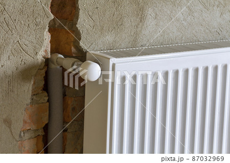 Close-up side view of isolated installed heating radiator on brick rough plastered wall in an empty room of a newly built apartment or house. Construction, maintenance, plumbing and repairing concept. 87032969