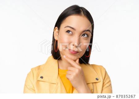 Close up of asian woman thinking, looking up thoughtful, pondering smth with pleased smiling face, standing over white background 87035267