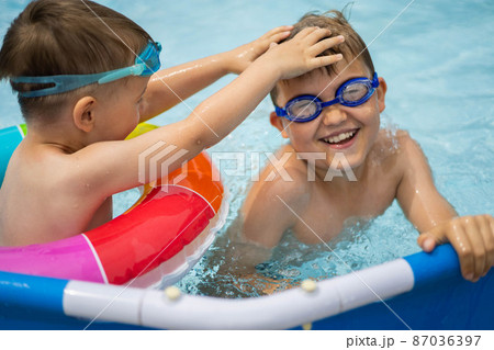 Two boys brothers in the outdoor outdoor pool near the house swim and play. Colored, swimming, bright, rainbow circles. Two boys brothers in the outdoor outdoor pool near the house swim and play. Colored, swimming, bright, rainbow circles. 87036397