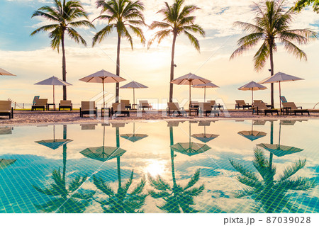 Beautiful luxury umbrella and chair around outdoor swimming pool in hotel and resort with coconut palm tree on sunset  or sunrise sky 87039028