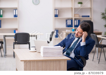 Young male employee and too much work in the office 87039979