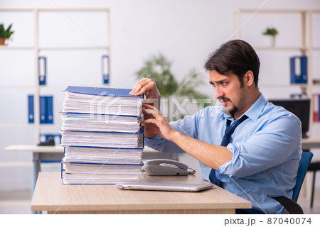 Young male employee and too much work in the office Young male employee and too much work in the office 87040074