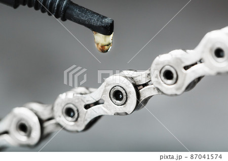 Greasing a bicycle chain with a drop of golden oil close-up on a gray background Greasing a bicycle chain with a drop of golden oil close-up on a gray background 87041574