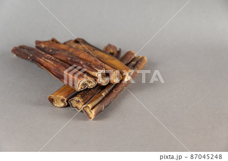 Pet chew treats. Natural dried dog treats against a gray background. Group of bully sticks. Pet supplies. 87045248