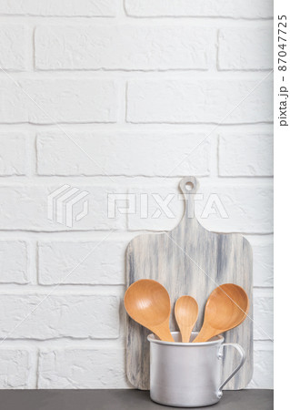 Kitchen background loft style. Kitchen utensils, dishes, wooden spoons in an aluminum mug on the background of a white brick rustic empty wall with copy space for text. Front view 87047725