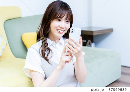 リビングでスマホを使う若い女性 87049686