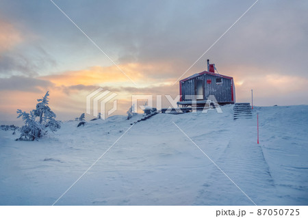 Cabin in winter dawn. Snow-covered staircase leading through snowdrifts to a lonely house on a hilltop in the cool evening. 87050725