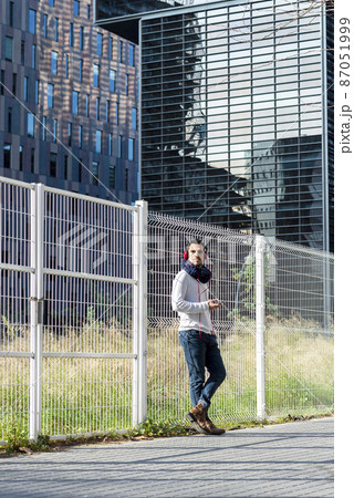 Young man listening music by headphones while holding a mobile phone outdoor 87051999