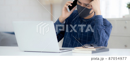Young asian business man in face mask talking smartphone and work on laptop computer. Young asian business man in face mask talking smartphone and work on laptop computer. 87054977