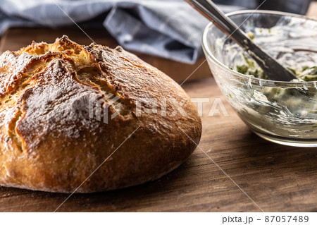 Crusty and soft bread loaf next to bowl of herb butter 87057489