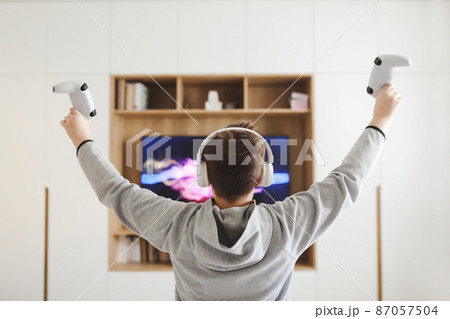 Boy in headphones watching television, teenager boy playing video game in front of screen at home 87057504
