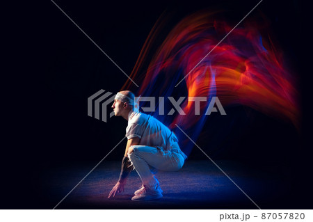 Sportive man in sports white suit dancing hip-hop isolated on dark background in mixed neon light. Youth culture, hip-hop, movement, style and fashion, action. 87057820