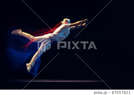 Portrait of man in sports white suit, hip-hop dancer flying isolated on dark background in mixed neon light. Youth culture, hip-hop, movement, style and fashion, action. 87057821