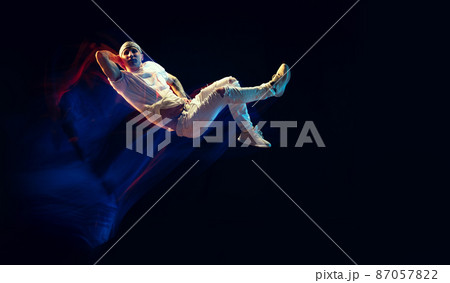Portrait of man in sports white suit, hip-hop dancer flying isolated on dark background in mixed neon light. Youth culture, hip-hop, movement, style and fashion, action. 87057822