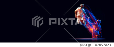 Portrait of man in sports white suit, hip-hop dancer flying isolated on dark background in mixed neon light. Youth culture, hip-hop, movement, style and fashion, action. 87057823