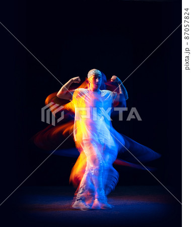 Sportive man in sports white suit dancing hip-hop isolated on dark background in mixed neon light. Youth culture, hip-hop, movement, style and fashion, action. 87057824