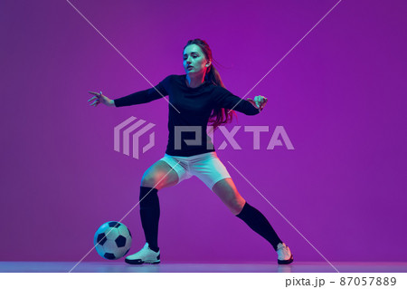 Professional female soccer player dribbling football ball isolated on purple studio background in neon light. Sport, action, motion, fitness Professional female soccer player dribbling football ball isolated on purple studio background in neon light. Sport, action, motion, fitness 87057889
