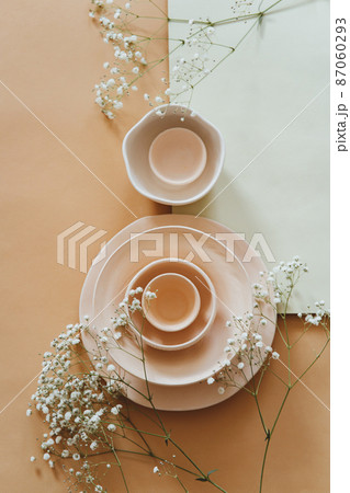 Ceramic bowls and delicate flowers on a beige and turquoise background 87060293
